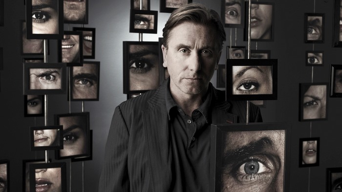 Tim Roth in front of framed eyes and faces