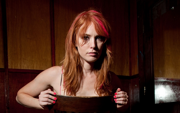 Alicia Witt sitting behind a wooden chair