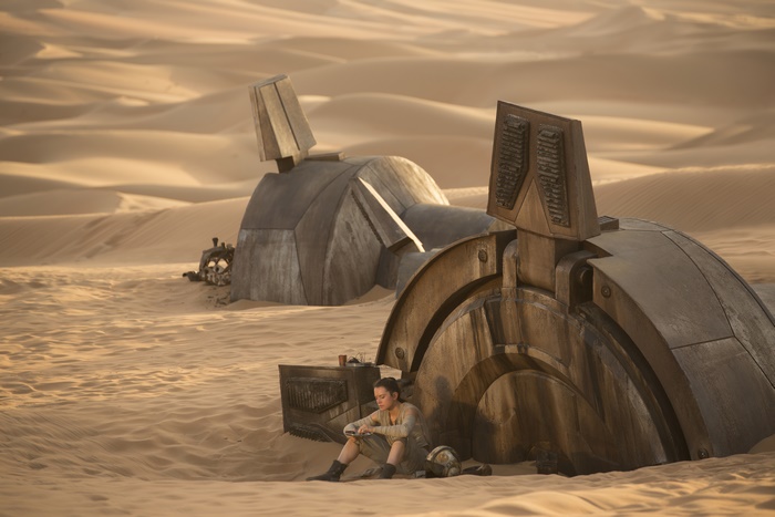 Rey from Star Wars sitting near wreckage in desert