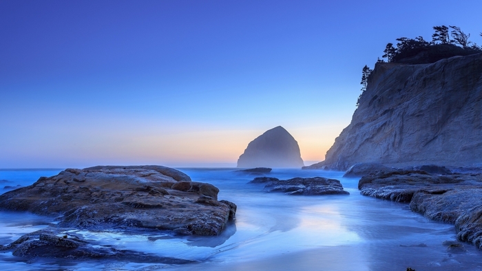 Ocean coast with rocks and a large sea stack at twilight