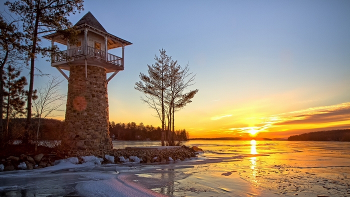 Stone lighthouse tower on frozen lake at sunset