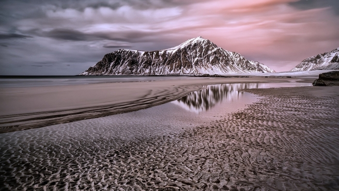 Snow-capped mountains reflected in a tidal pool on a beach