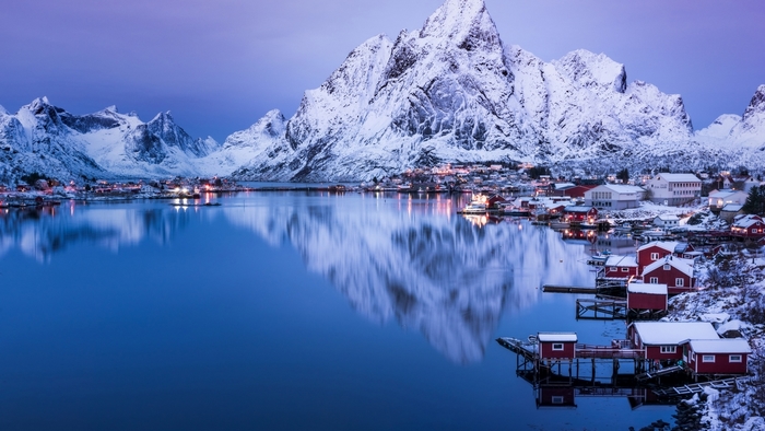 Snowy mountains and village reflected in a calm lake