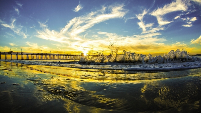 Sunset over the ocean with waves and a pier
