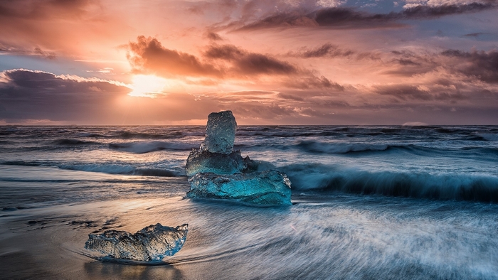 Icebergs on a beach at sunrise with dramatic clouds