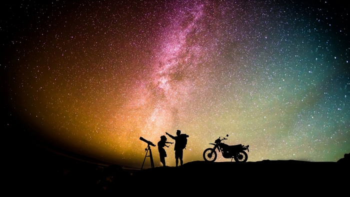 Couple stargazing with a motorcycle under the Milky Way
