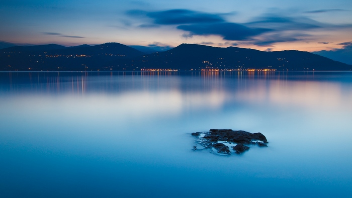Calm lake at dusk with mountain silhouette and lights