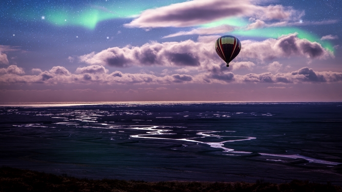 Hot air balloon flying under aurora borealis over water