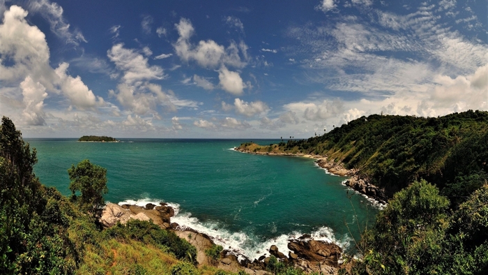 Tropical bay with island and lush green hills under a cloudy sky