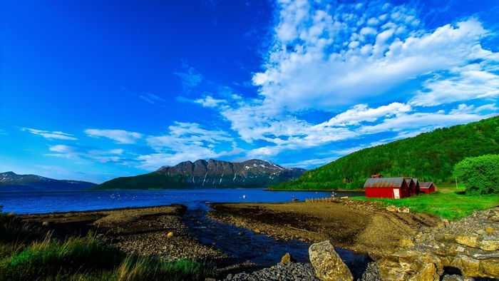 Red cabins by a lake with mountains and blue sky
