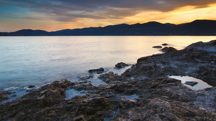 Rocky shoreline at sunset with mountains in the background