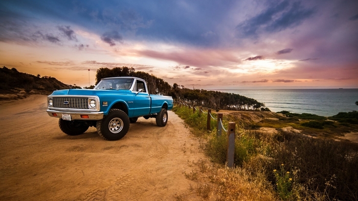 Blue lifted Chevrolet pickup truck on dirt road at sunset