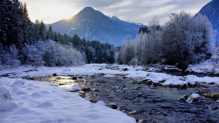 Snowy river flowing through a winter forest with mountains