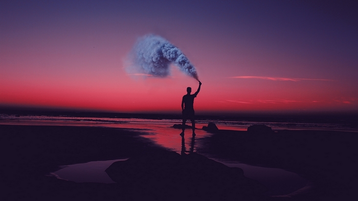 Man holding smoke bomb on beach at sunset