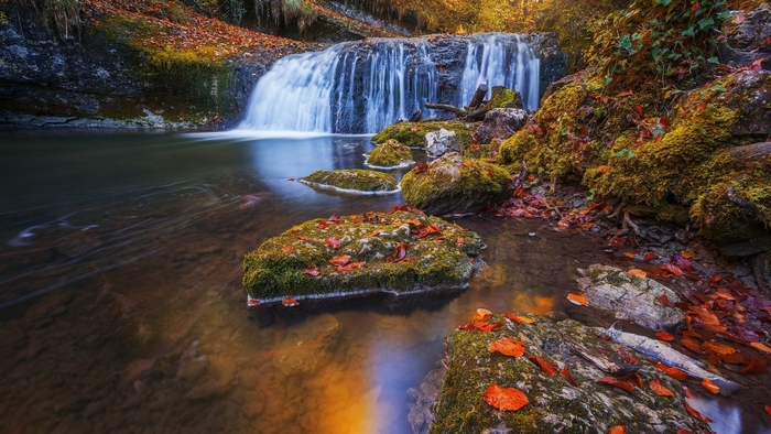 Waterfall flowing over mossy rocks in autumn forest