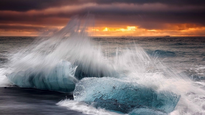 Waves crashing on icebergs at sunset