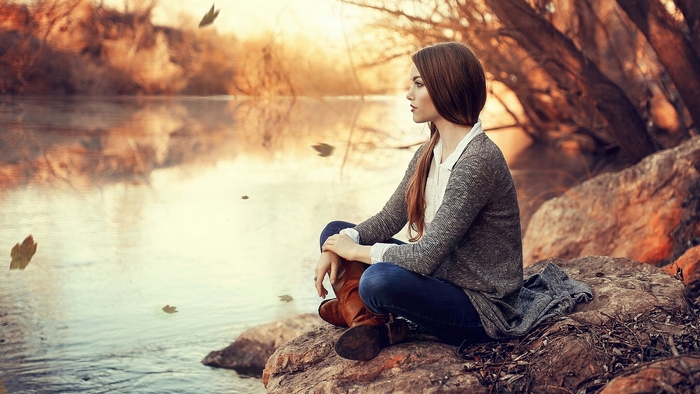 Woman in autumn clothes sitting by a river