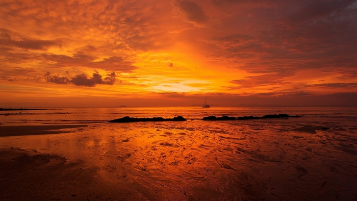Sunset over the ocean with a sailboat and beach
