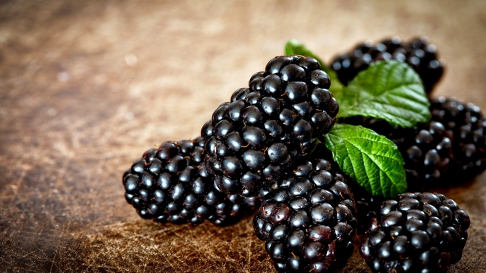 Blackberries with green leaves on a wooden surface