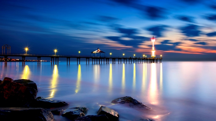 Pier with lights reflecting on the ocean at sunset