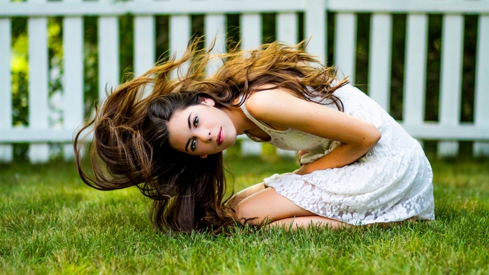 Young woman with long brown hair kneeling on grass