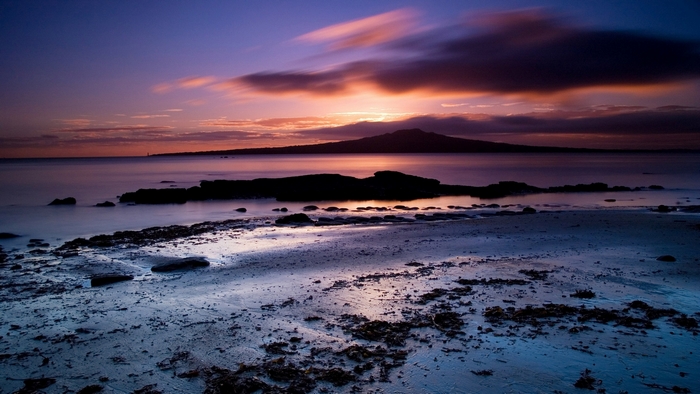 Sunset over water with mountain silhouette and beach