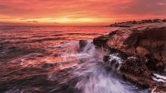 Sunset over rocky coast with waves crashing