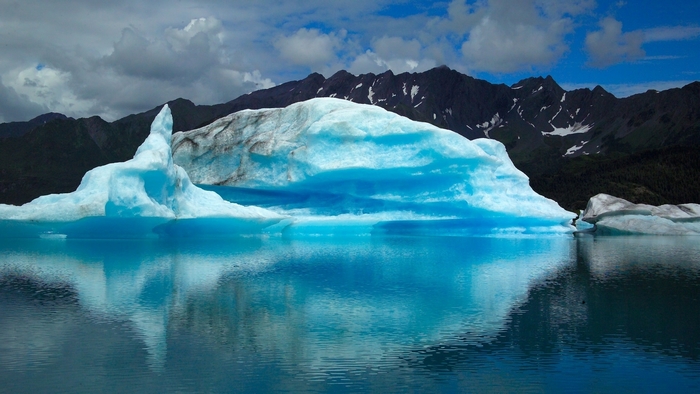 Blue icebergs floating in a lake with mountains in the background