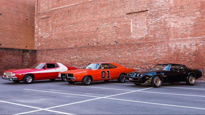 Three classic American muscle cars parked in front of a brick wall