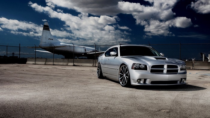 Silver Dodge Charger parked near an airplane