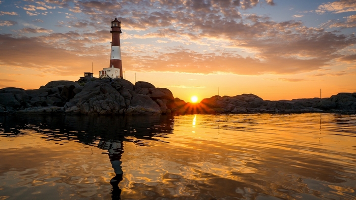Lighthouse on rocky coast at sunset with reflection