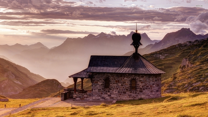 Small stone chapel on a grassy mountain slope at sunset
