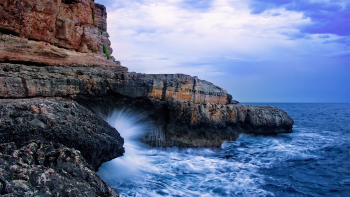 Waves crashing against rocky cliffs under a cloudy sky