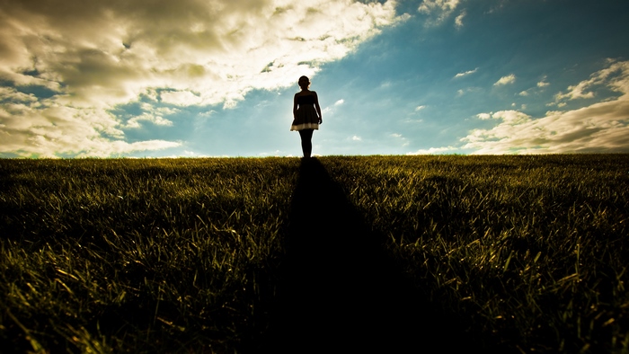 Girl walking on a grassy hill under cloudy sky