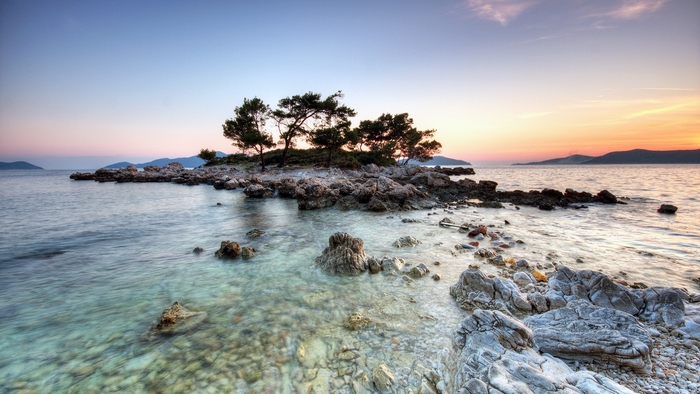 Rocky island with trees at sunset over the ocean