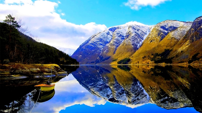Snow-capped mountains reflected in a calm lake with a boat