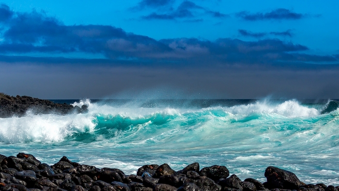 Turquoise waves crash on a rocky shore under a blue sky