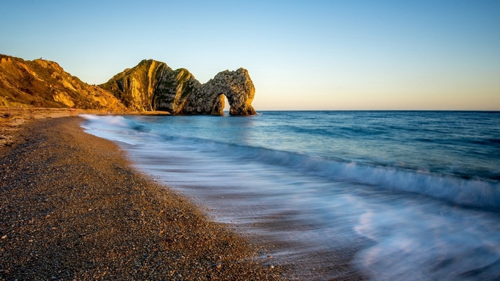 Durdle Door rock arch on a pebble beach at sunset