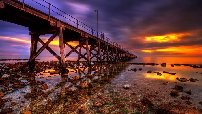 Wooden pier over rocky shore at sunset