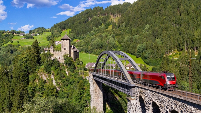 Train crossing a bridge near a castle in the Alps