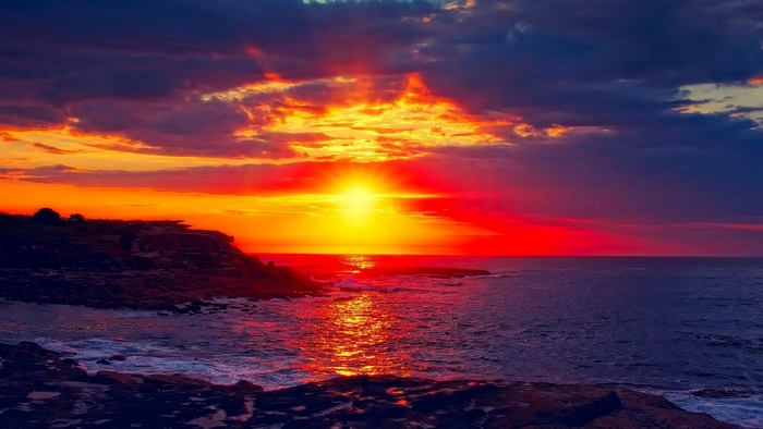 Vibrant Sunset Over Rocky Beach with Cloudy Sky