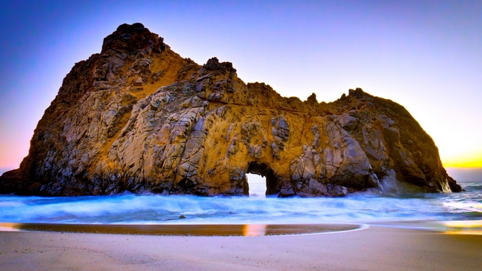 Rock arch with waves on a beach at sunset