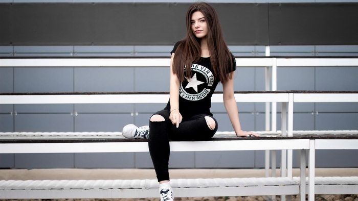 Young woman in ripped jeans sitting on bleachers
