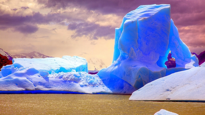 Blue iceberg in a lake with mountains and clouds