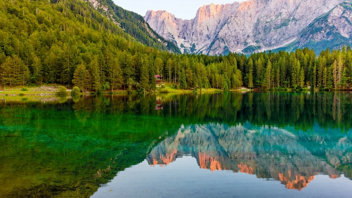 Emerald lake reflecting mountains and forest in Italy