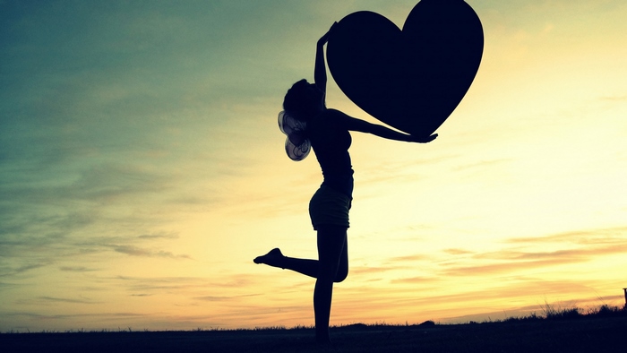 Silhouette of a girl holding a heart against the sunset