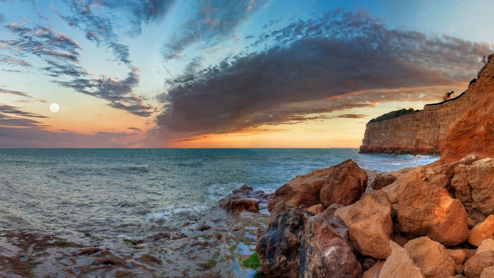 Sunrise over the ocean with rocky cliffs and moon