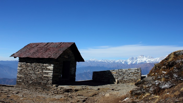 Stone shelter with snow-capped mountains under a blue sky