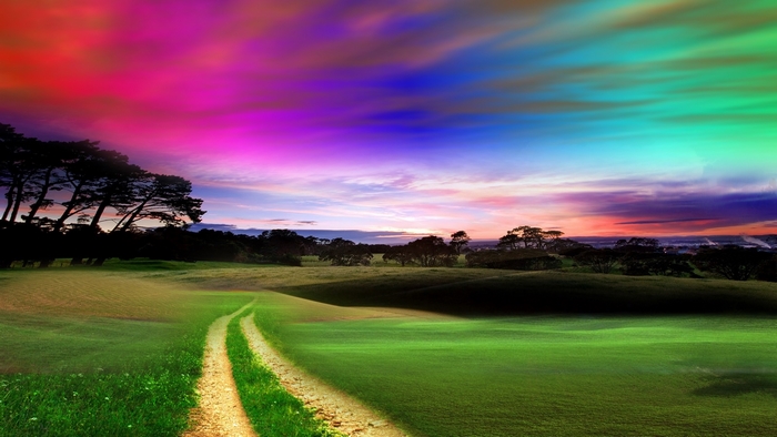 A winding dirt path through a green field under a colorful sky