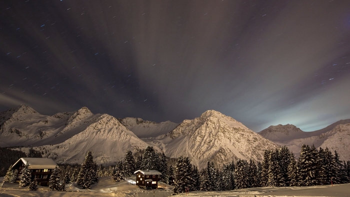 Snowy mountains and cabins at night with star trails